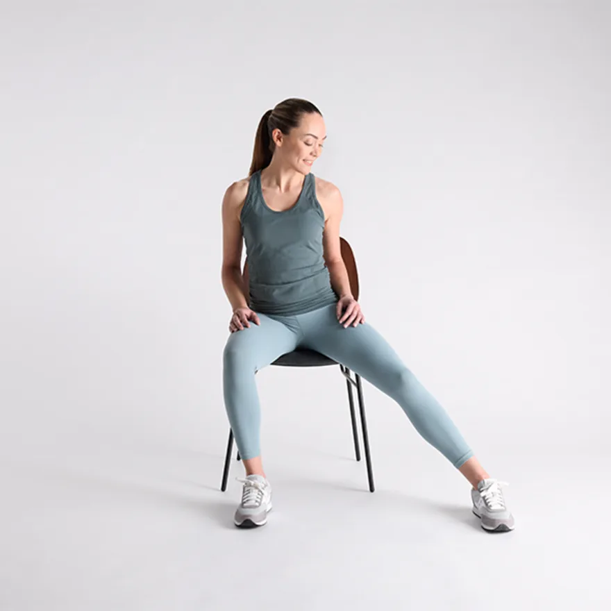 Person in blue-gray workout attire sitting on chair demonstrating addcutor exercises