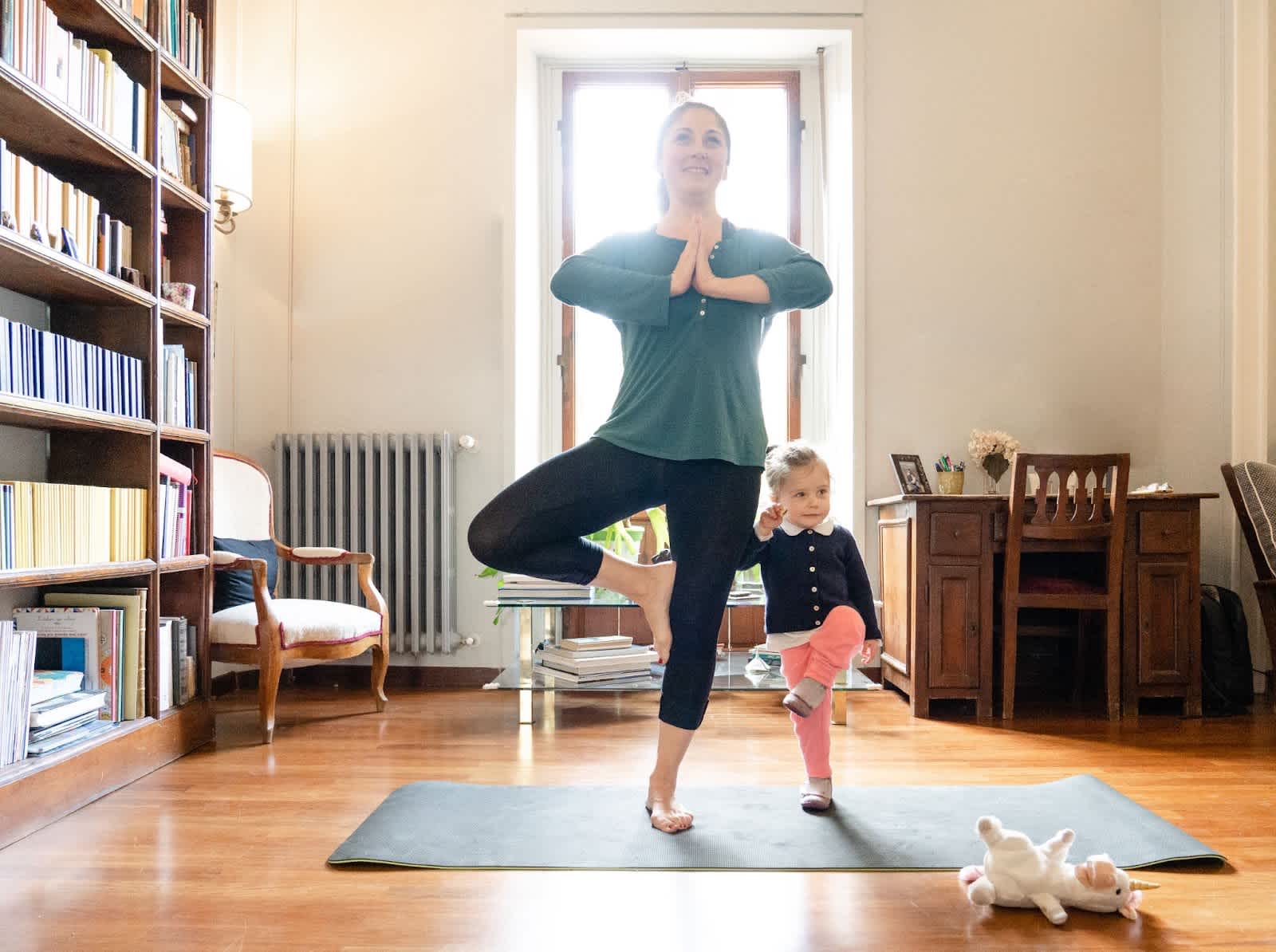 Image of woman doing a yoga pose with a child standing next to her. 