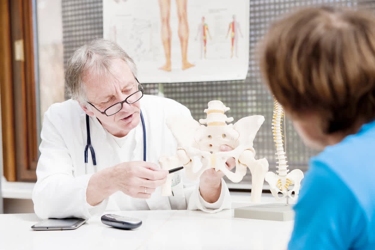 Doctor-holding-plastic-skeleton-of-the-pelvis-to-show-his-patient-at-appointment