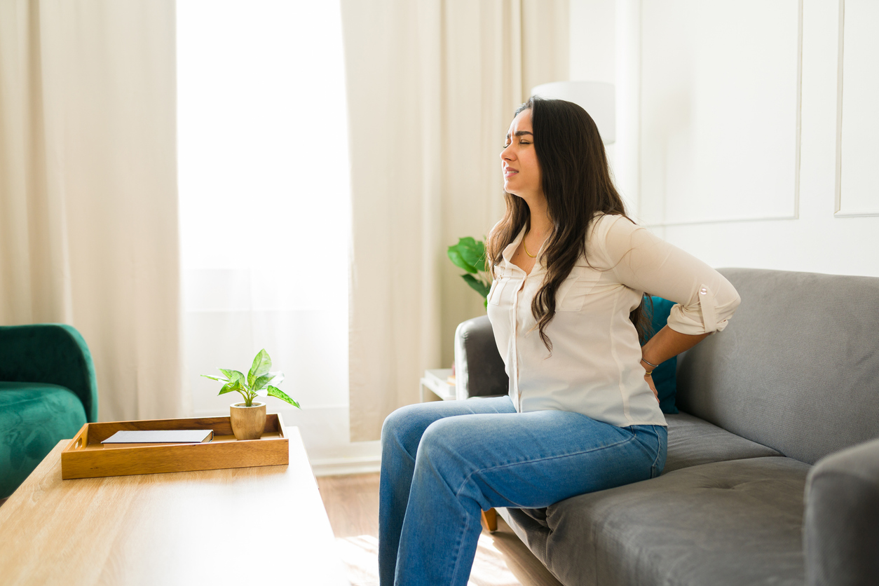 Person sitting on gray couch experiencing back pain and wondering how to sit with sciatica pain 