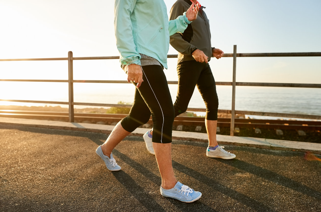 Image of two women dressed in warm layers, walking along a path with the ocean in the background