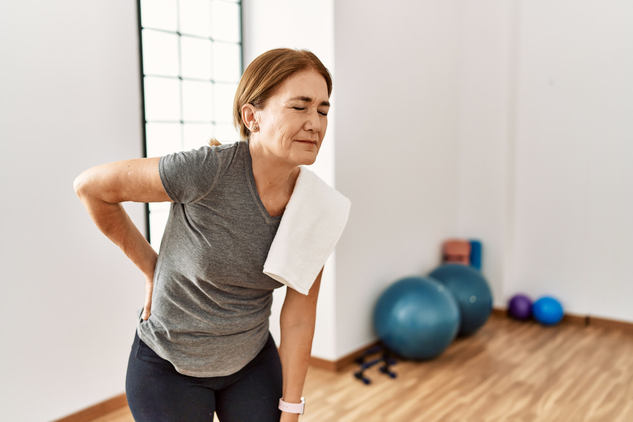 Person in workout clothes experiencing DOMS and needing treatment with exercise equipment visible in background