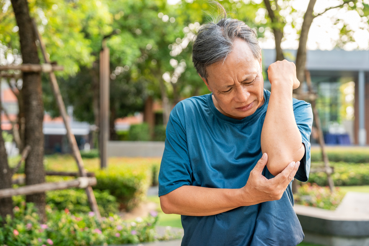 Person in blue t-shirt grimacing while holding their elbow in pain due to elbow bone spur.