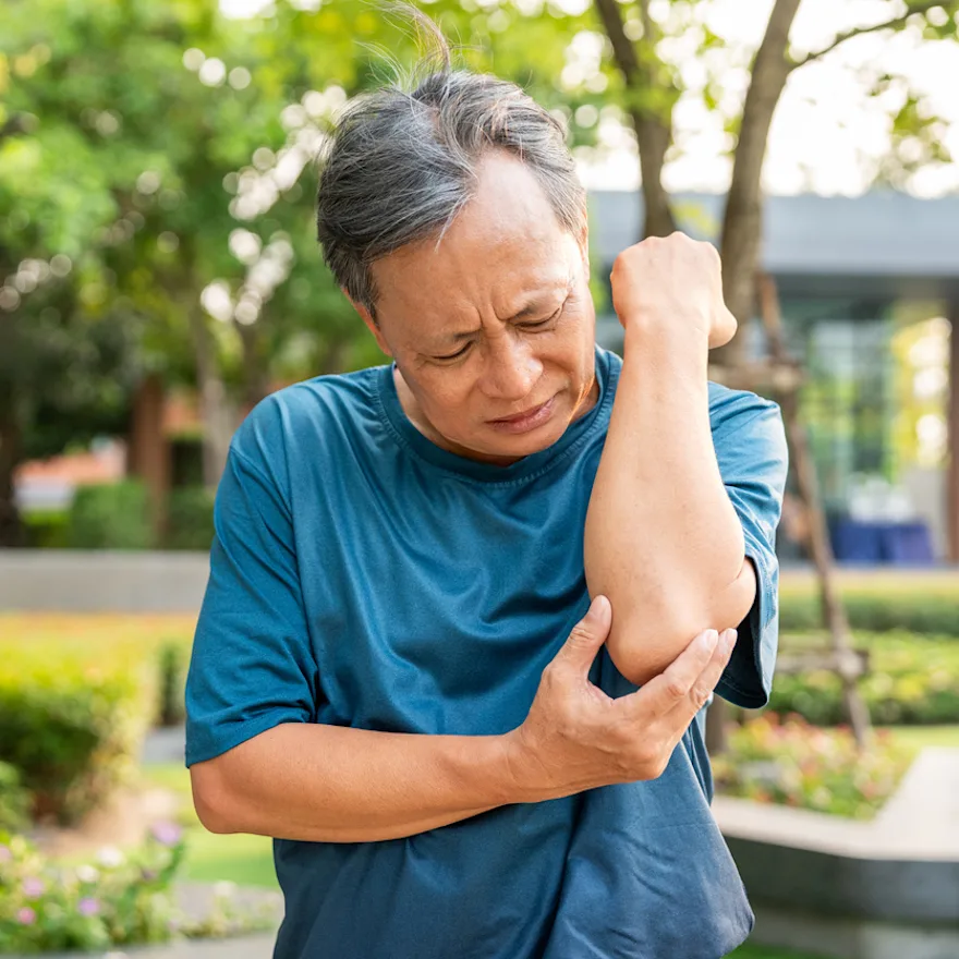 Person in blue t-shirt grimacing while holding their elbow in pain due to elbow bone spur.