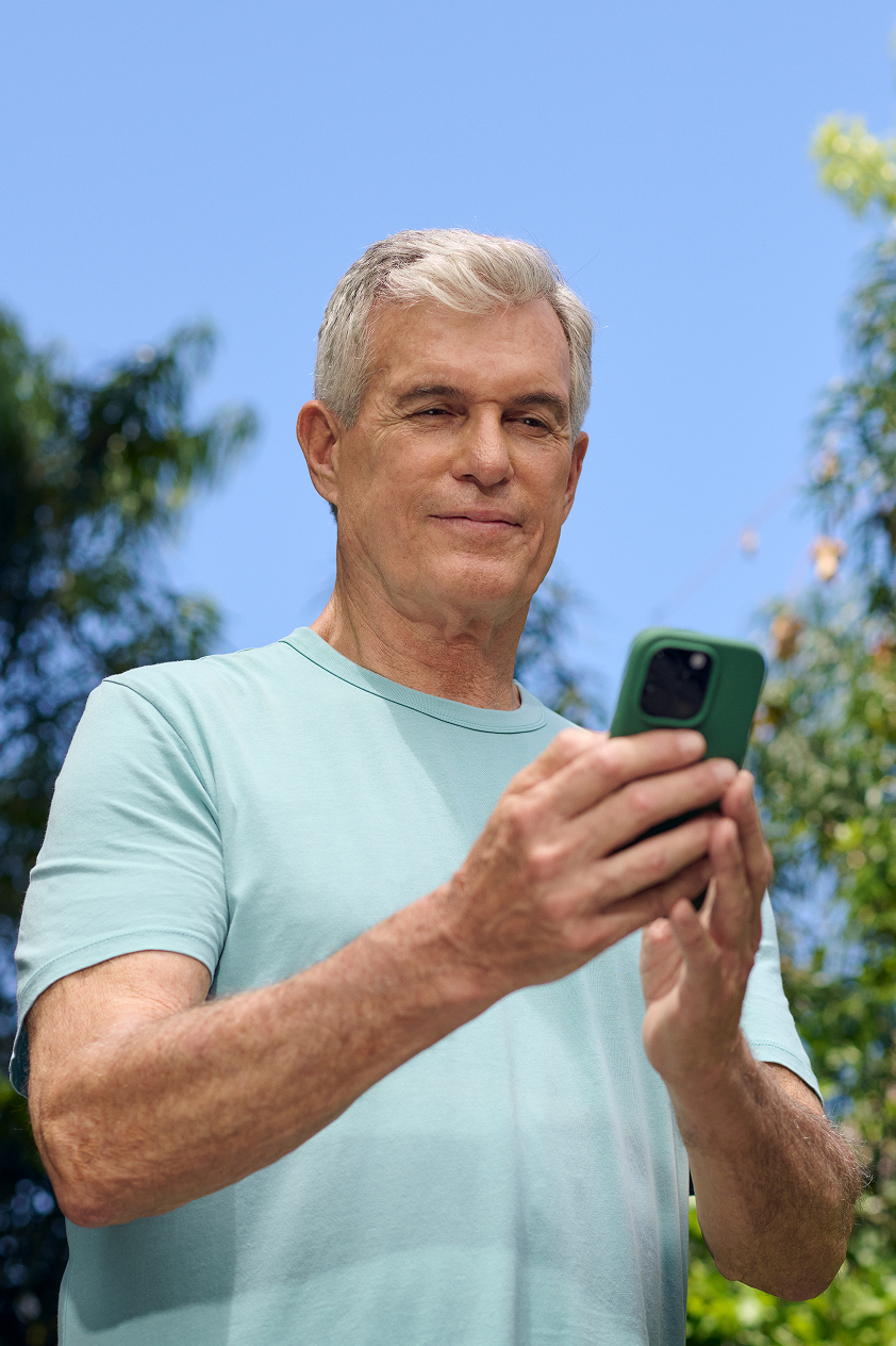 A man is checking his phone outdoors and confirming his upcoming Hinge Health video call with a physical therapist.
