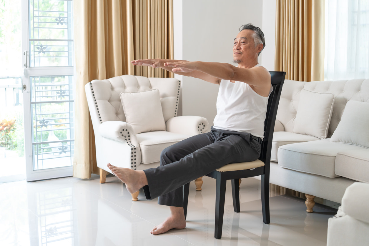 Senior man performing ilitobilial band syndrome exercises in bright living room with white sofa and beige curtains