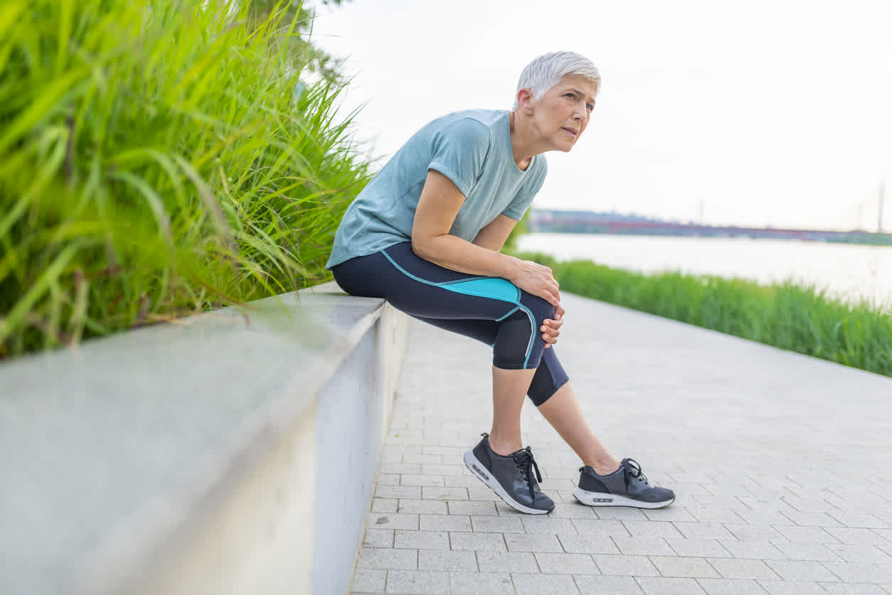elderly-woman-touching-knee-in-pain-while-walking-outdoors