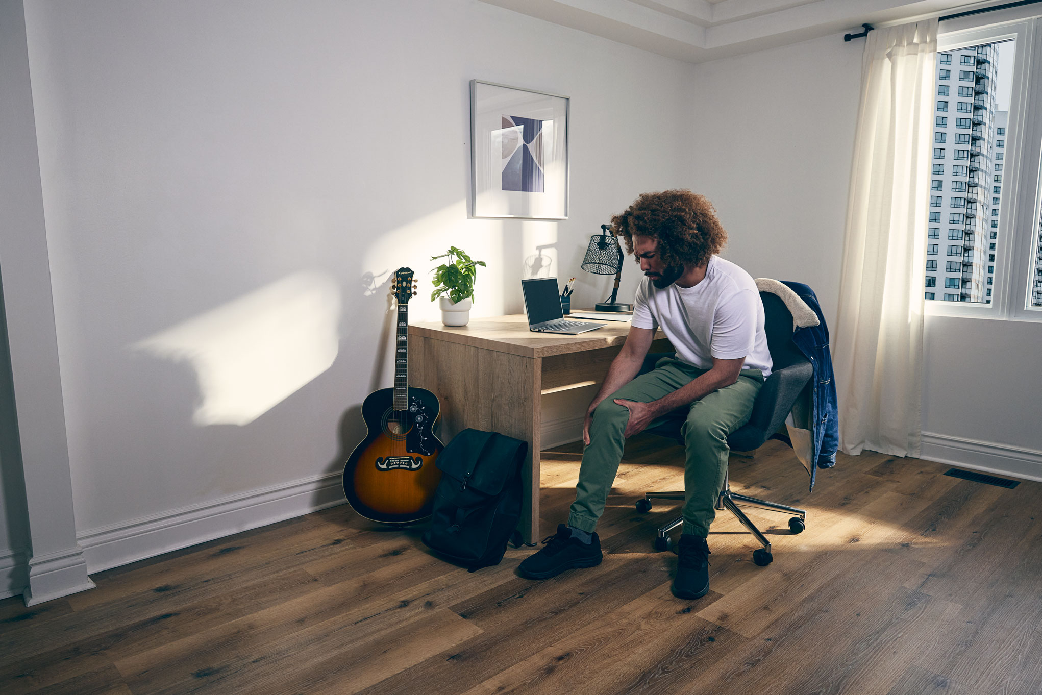Man-sitting-at-his-desk-at-home-grabbing-knee-in-pain