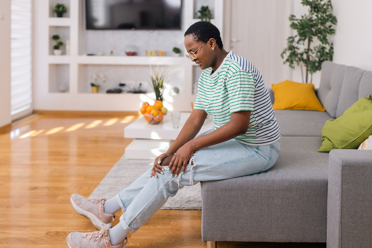 womna-touching-her-knee-in-pain-sitting-at-home