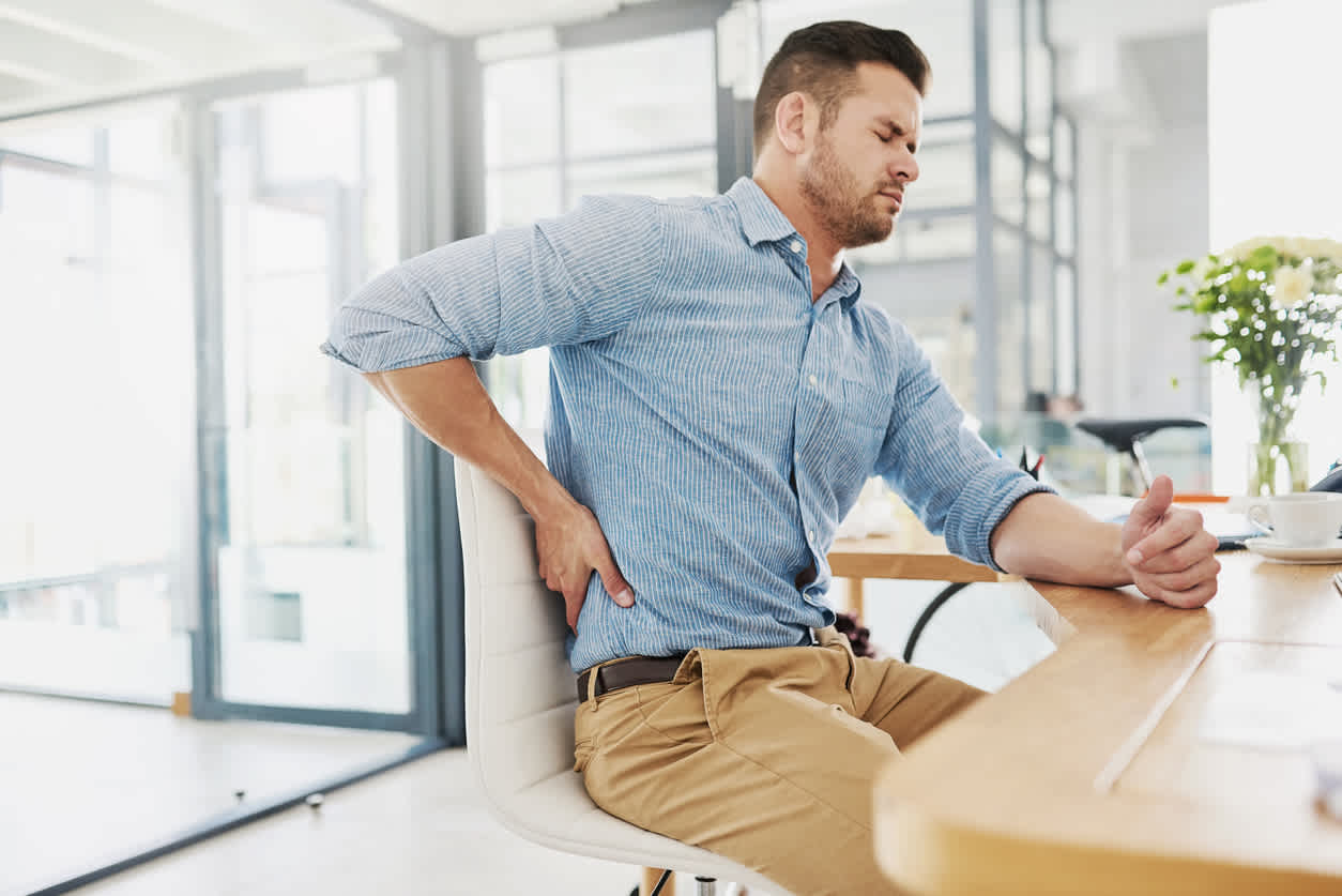 Man-sitting-at-desk-touching-his-lower-back-in-pain