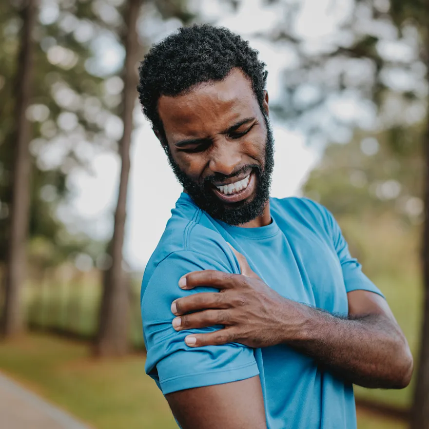 Person in blue athletic shirt grimacing while holding their shoulder feeling burning pain.