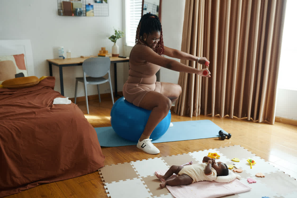 woman-exercising-in-ball-next-to-her-baby