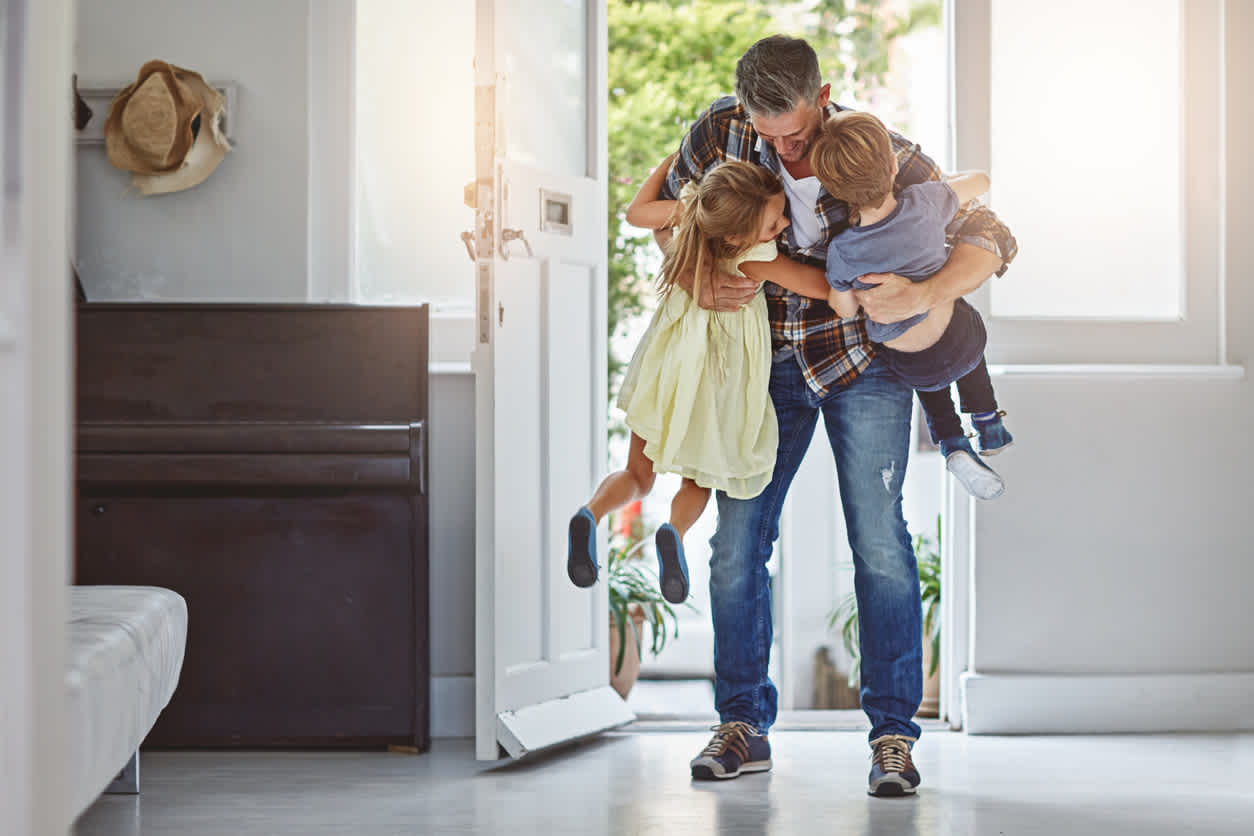 Image of man bending over and picking up two kids. 