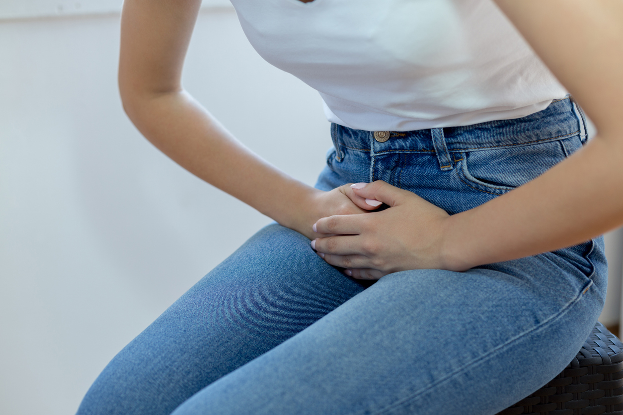 Person in white shirt and jeans holding their stomach in pain due to urinary retention. 