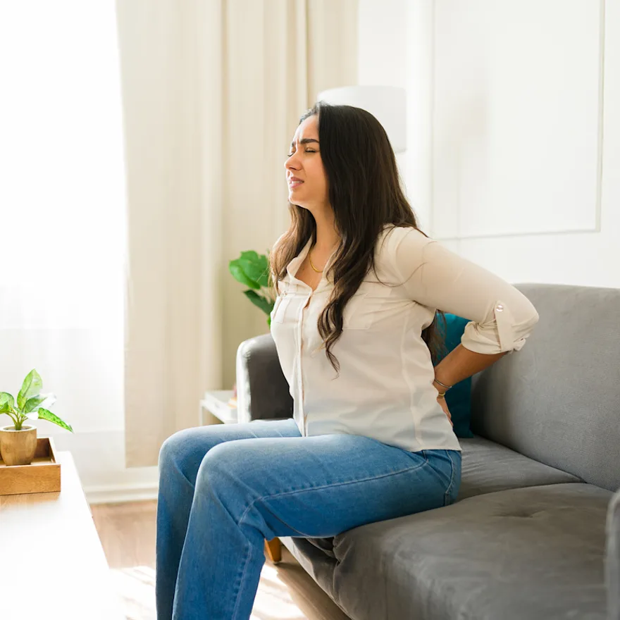 Person sitting on gray couch experiencing back pain and wondering how to sit with sciatica pain