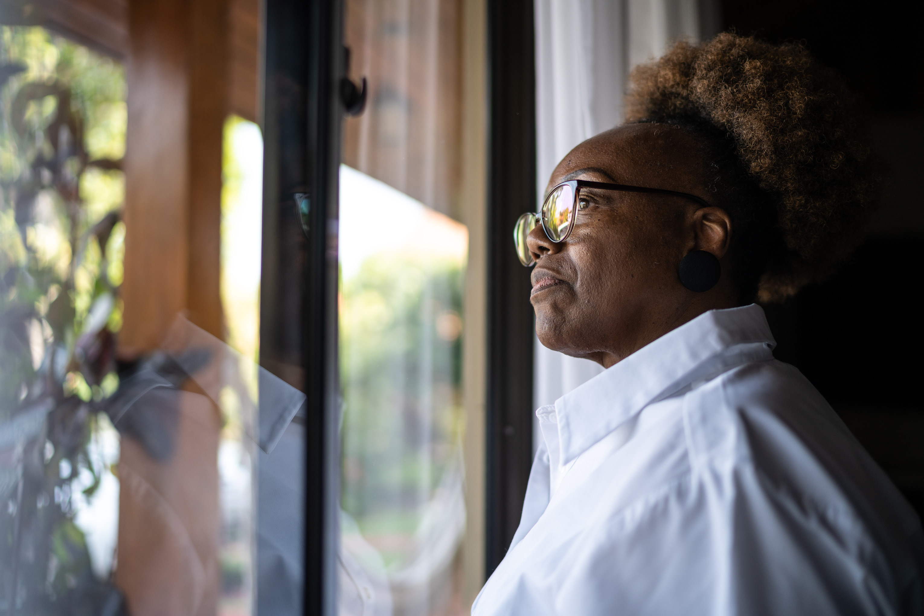 Photo of a woman with a contemplative expression, gazing out of her window