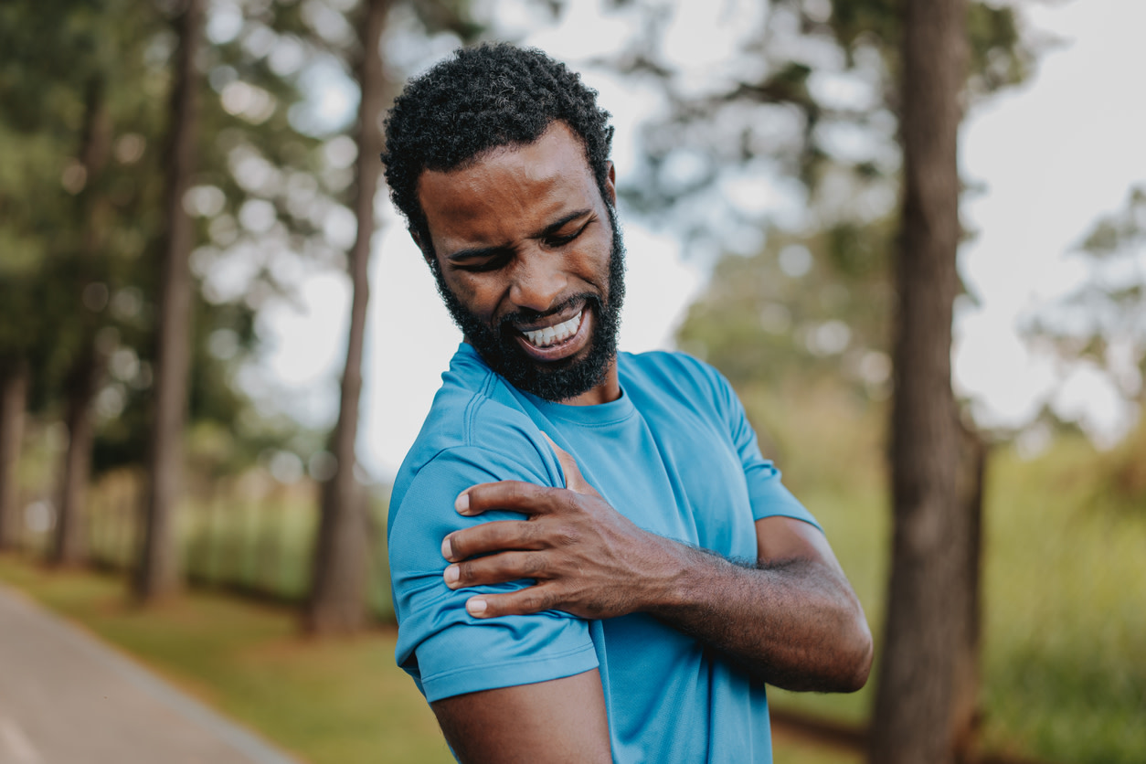 Person in blue athletic shirt grimacing while holding their shoulder feeling burning pain.