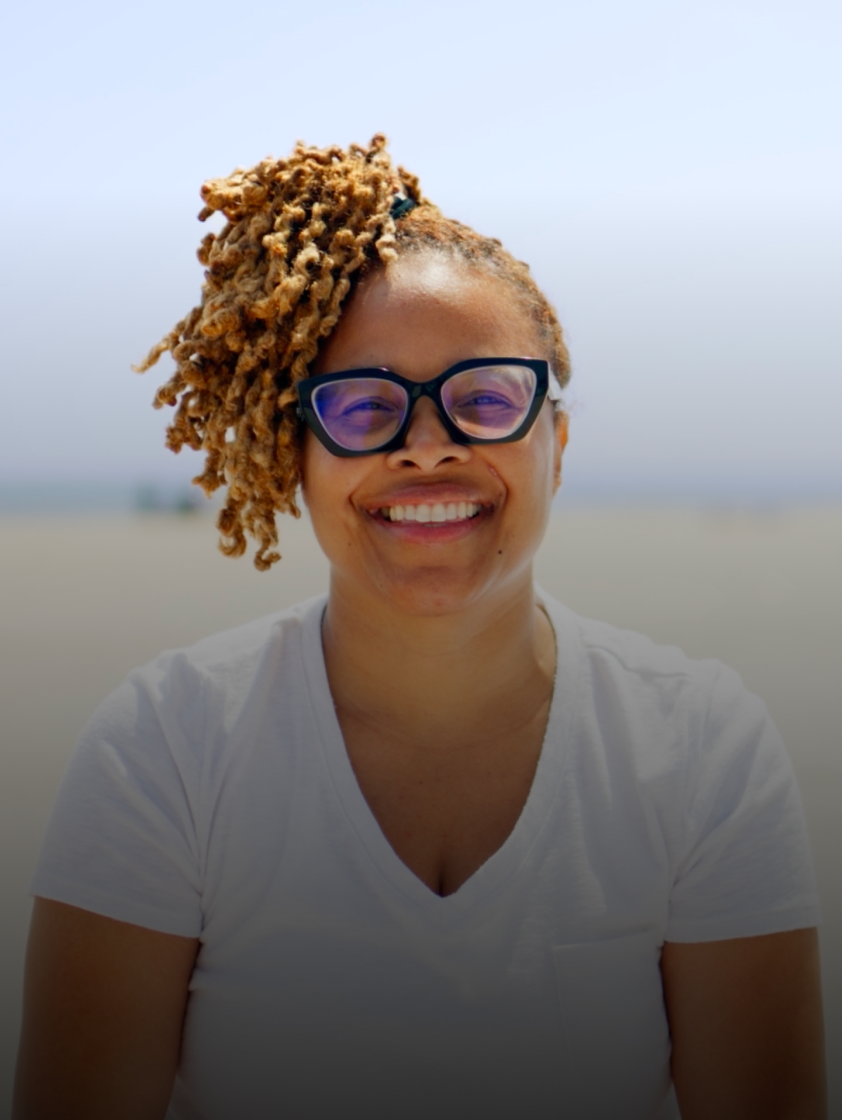 A woman is smiling at the beach and is sharing how Hinge Health improved her life in a video testimonial.