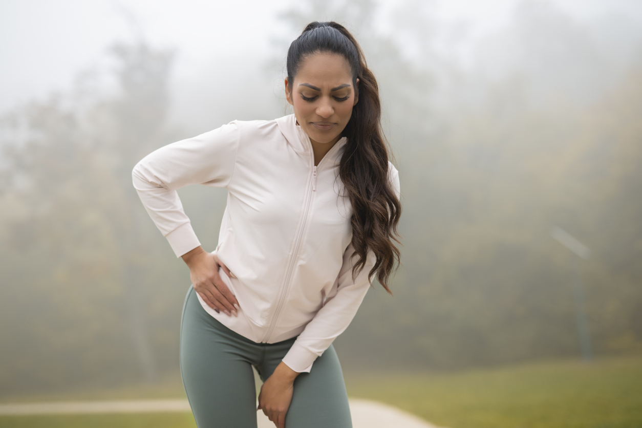 Person in white zip-up jacket and green leggings experiencing pain in front of hip.