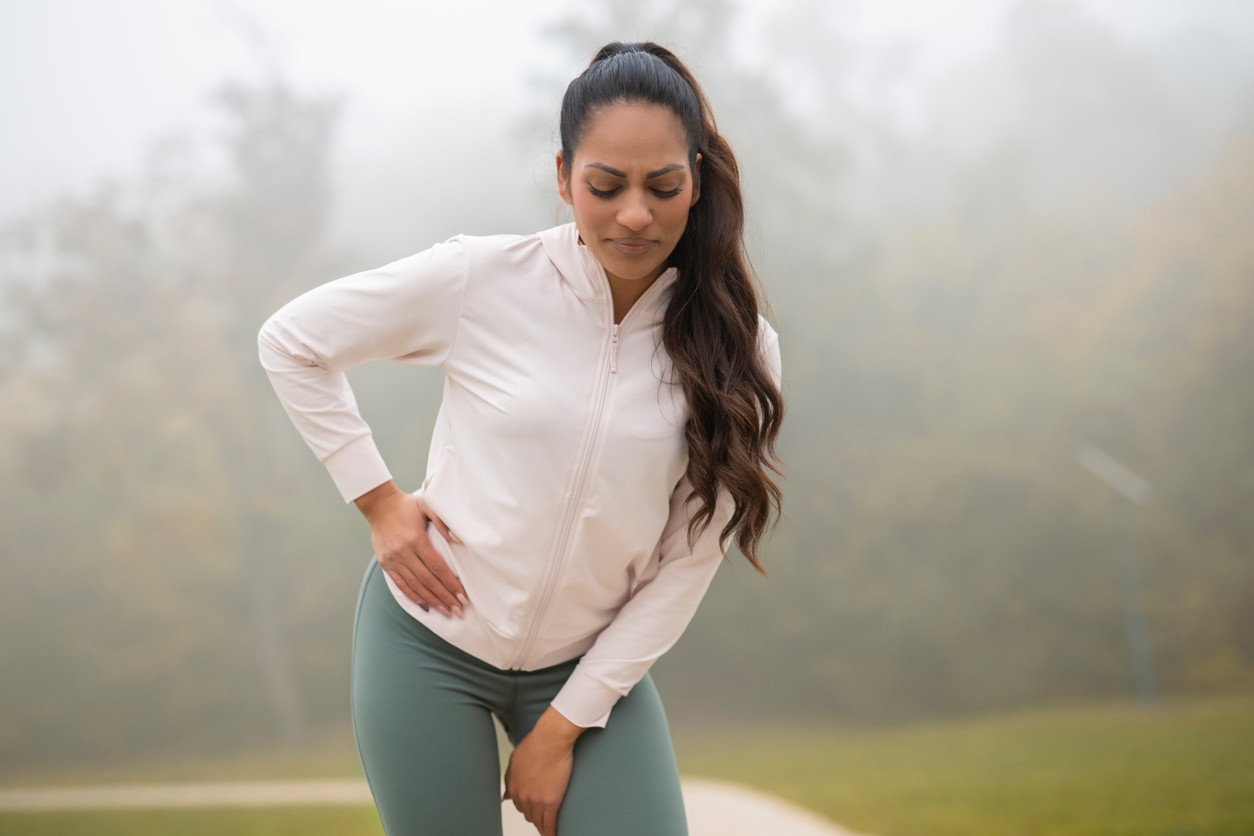 Person in white zip-up jacket and green leggings experiencing pain in front of hip.