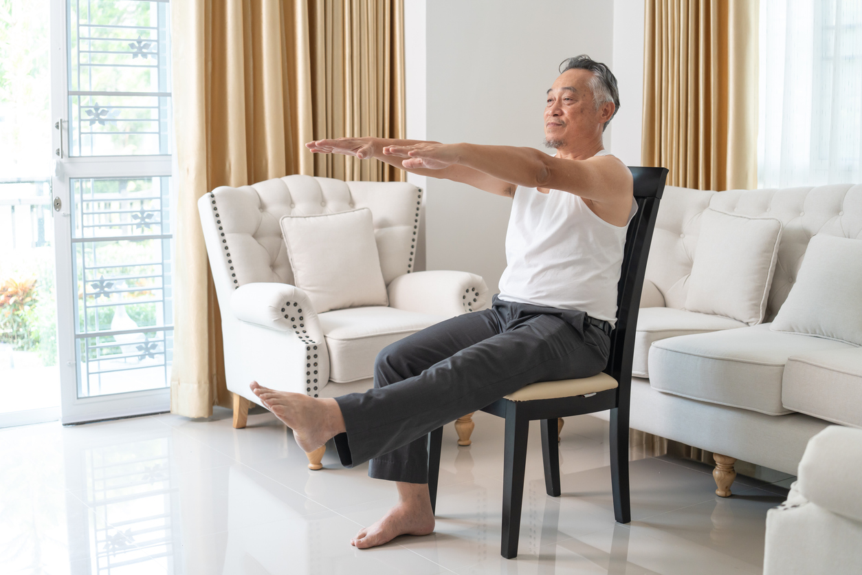 Senior man performing ilitobilial band syndrome exercises in bright living room with white sofa and beige curtains
