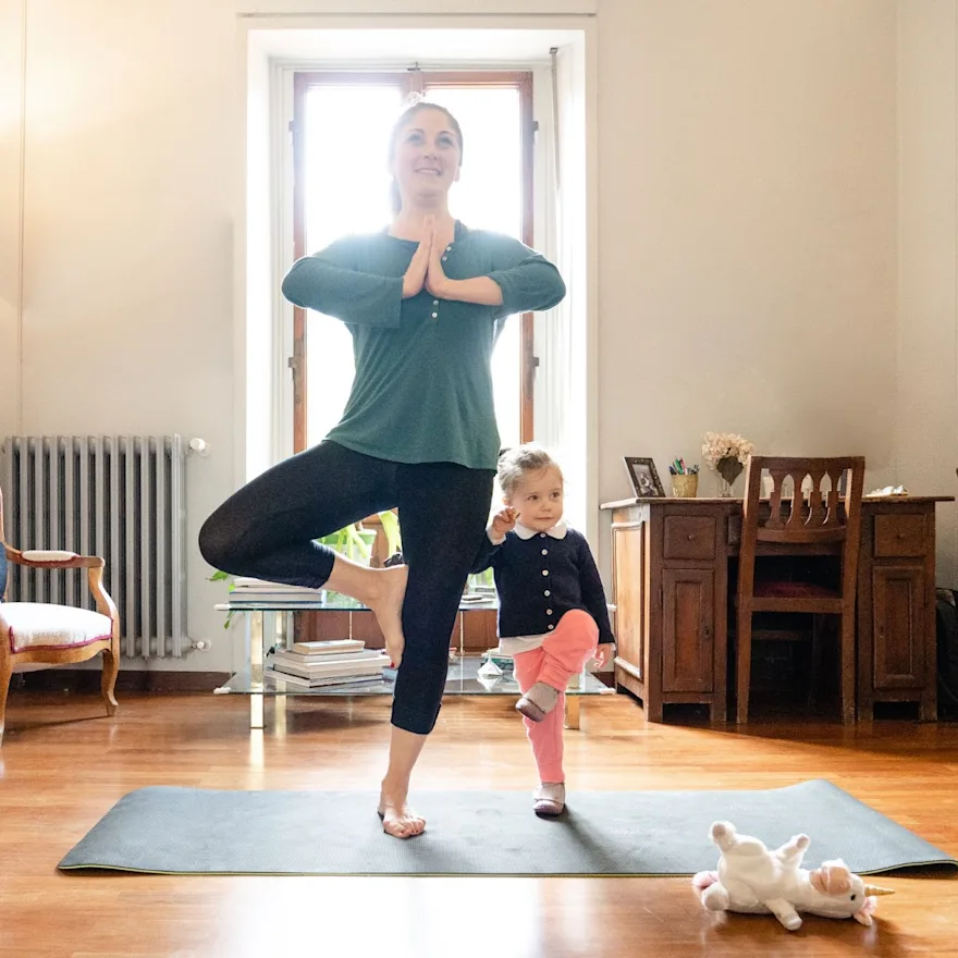 Woman doing yoga pose with child standing next to her