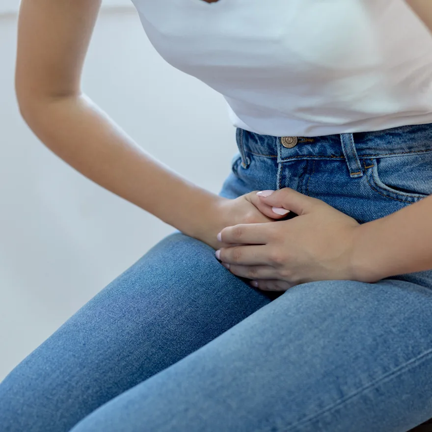 Person in white shirt and jeans holding their stomach in pain due to urinary retention.