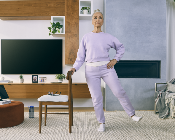 Elderly-woman-doing-side-leg-lift-leaning-on-chair-at-home