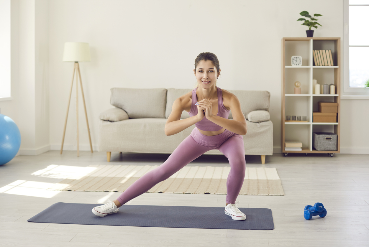 Person in purple doing dynamic balance exercises on exercise mat in bright living room with fitness equipment nearby