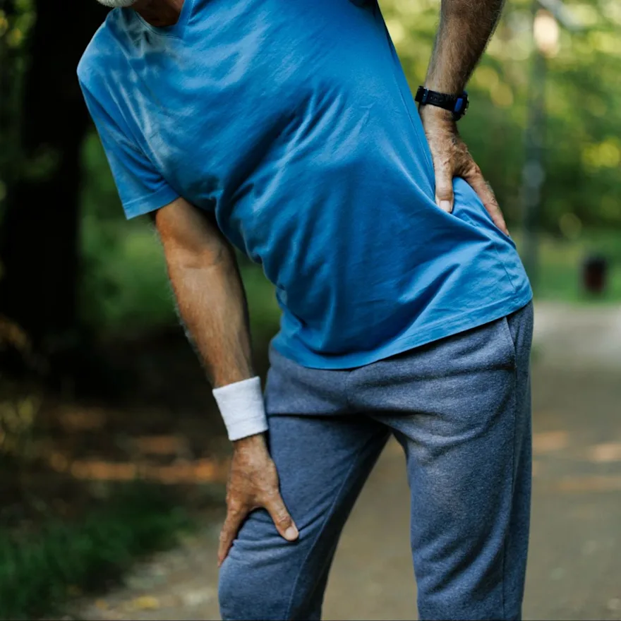 Person in blue t-shirt and sweatpants holding their hip in pain due to referred pain.