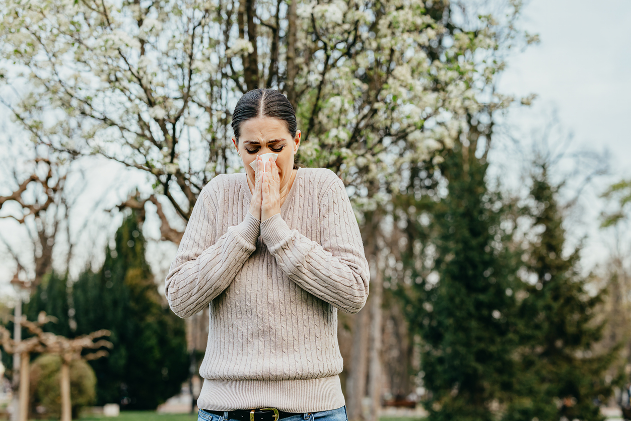 Woman in beige cable knit sweater sneezing and experiencing stress incontinence. 