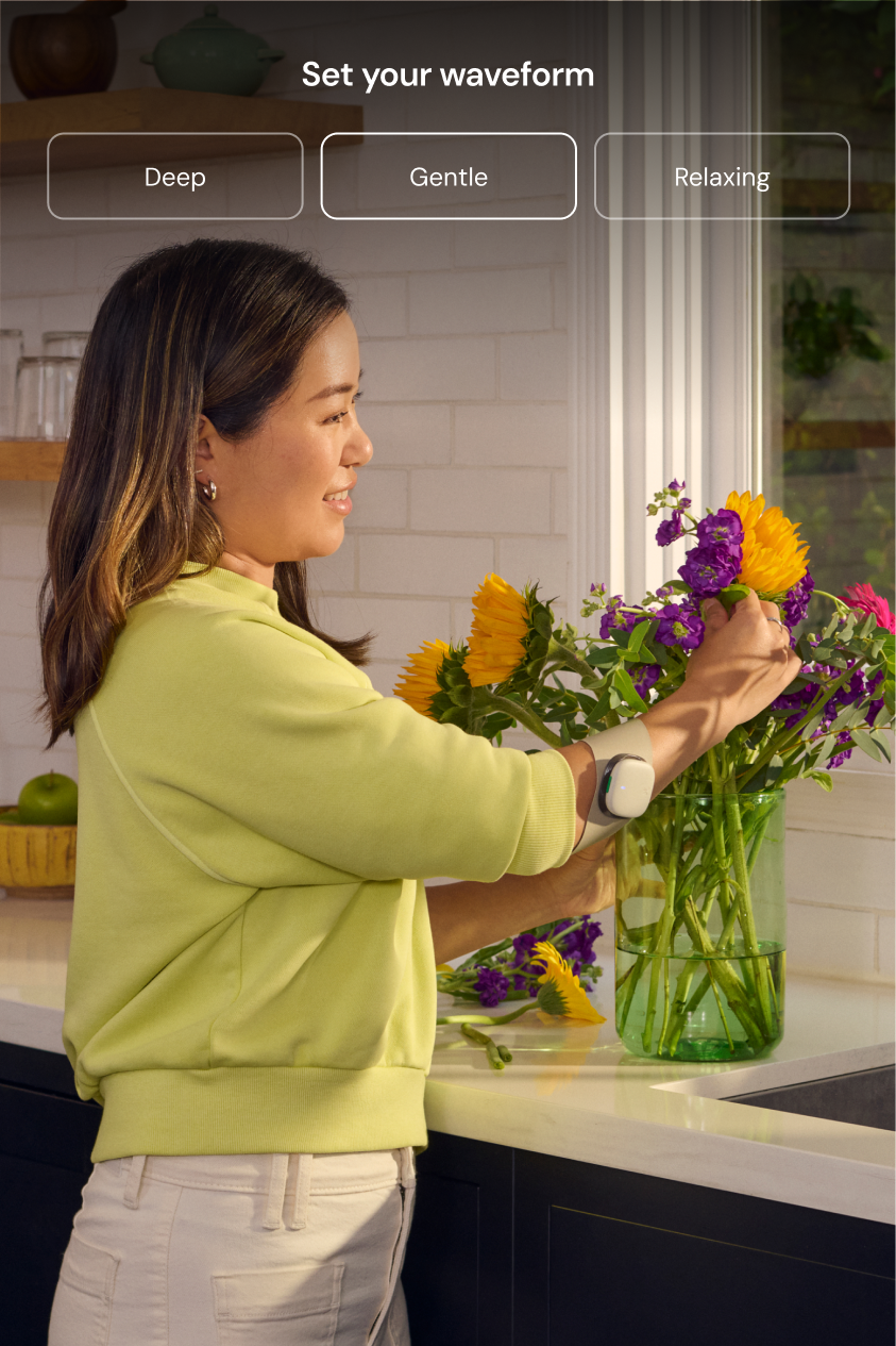 A woman is arranging flowers in her kitchen while wearing Enso on her arm, providing pain relief.