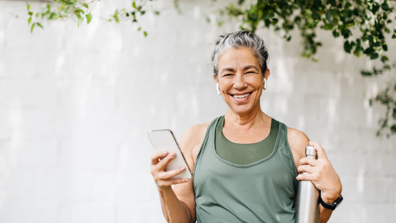 woman-smiling-holding-phone-and-bottle-in-exercise-clothes