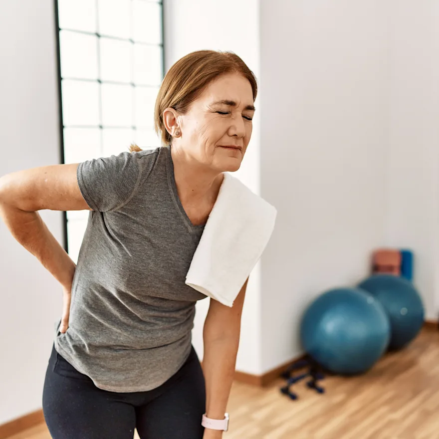 Person in workout clothes experiencing DOMS and needing treatment in an exercise room with fitness equipment visible.