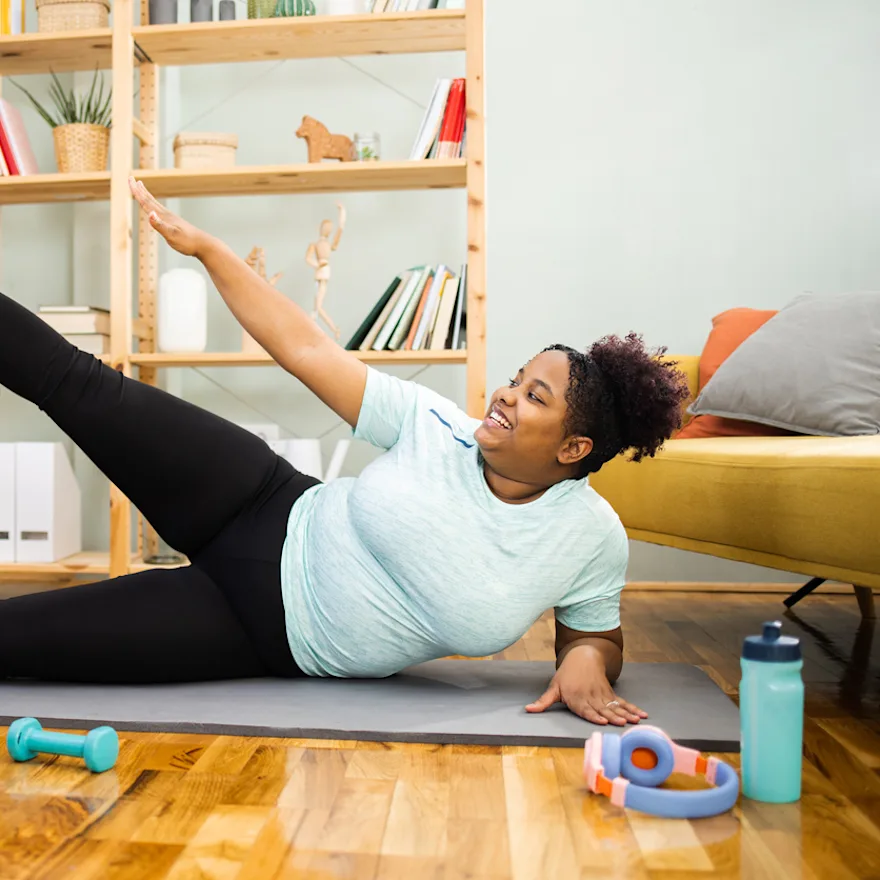 Woman exercising on yoga mat at home, performing gluteus medius exercises.