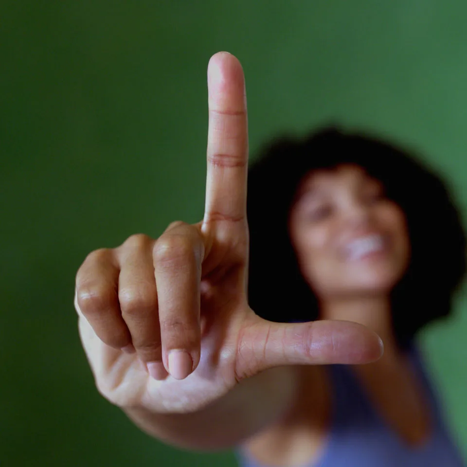 Smiling woman holding up her hand in the letter “L.” to represent the brand “L.”