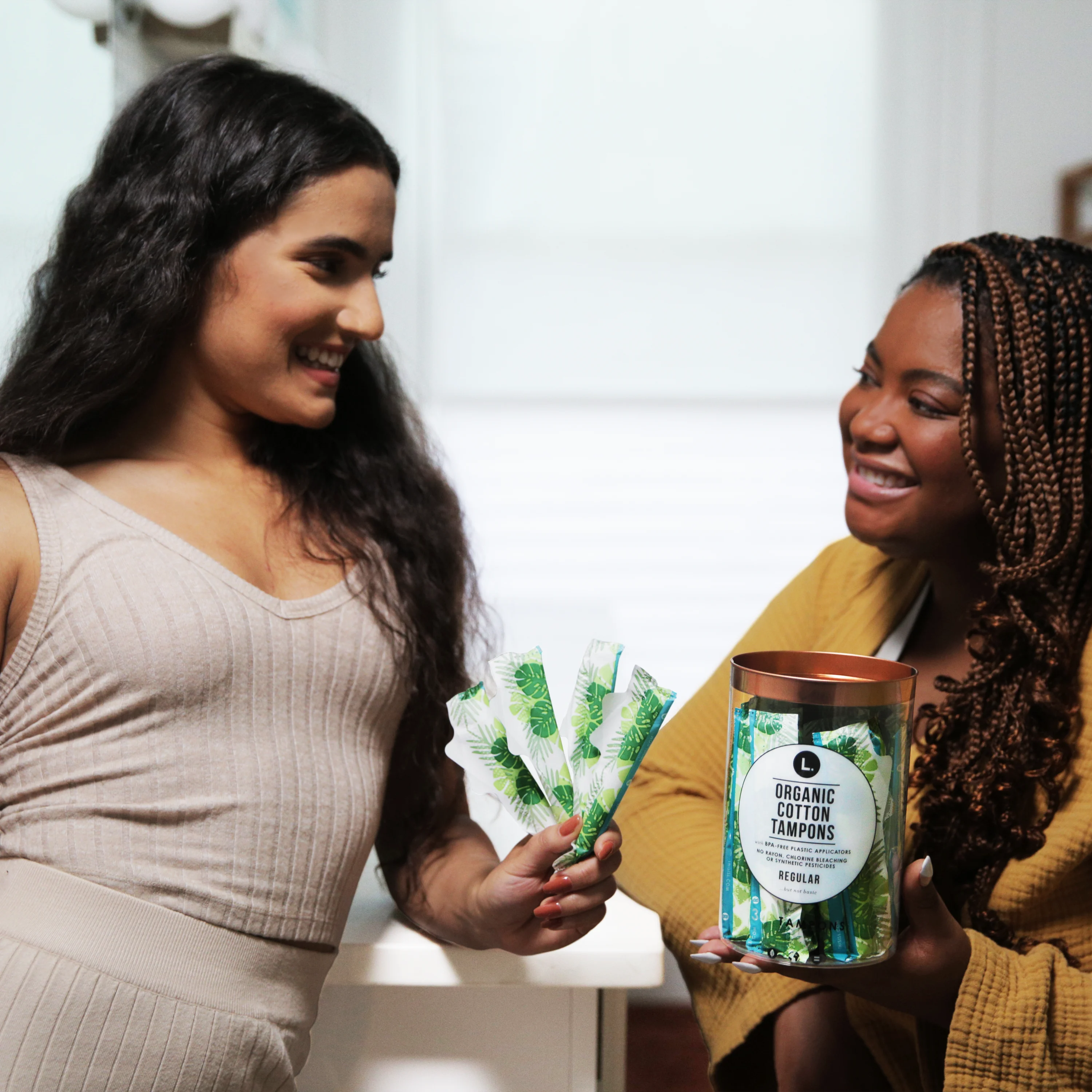 Two women standing next to each other holding a pack of tampons. 