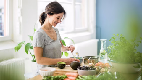 A young woman cuts up avocado in the kitchen while smiling A young woman cuts up avocado in the kitchen while smiling