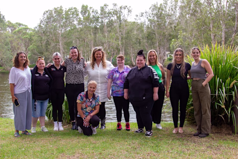 Eleven female participants of We Care's Sista Circle program standing outdoors by the river smiling Eleven female participants of We Care's Sista Circle program standing outdoors by the river smiling