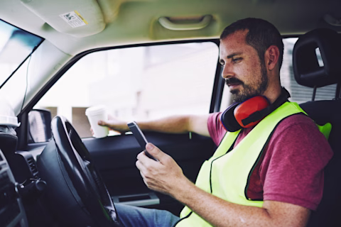 Construction worker texting on the phone inside a stationary car Construction worker texting on the phone inside a stationary car