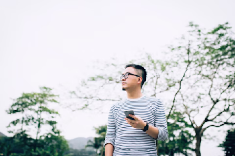 Smart young man using mobile phone while strolling and relaxing in park Smart young man using mobile phone while strolling and relaxing in park