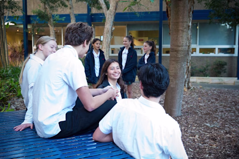 A group of teenagers in school uniform sitting together on and around a table, smiling and talking to each other. A group of teenagers in school uniform sitting together on and around a table, smiling and talking to each other.