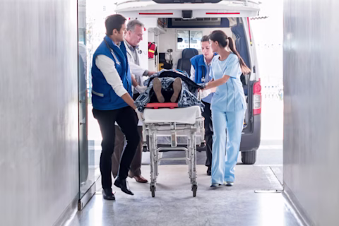 Paramedics push a stretcher out the back of an ambulance down the hallway of a hospital