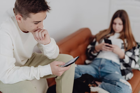 Two teenagers sitting on a couch, each looking at their own mobile Two teenagers sitting on a couch, each looking at their own mobile