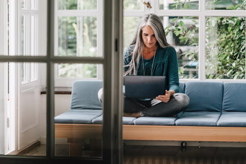 Woman sitting on lounge in winter garden using laptop Woman sitting on lounge in winter garden using laptop