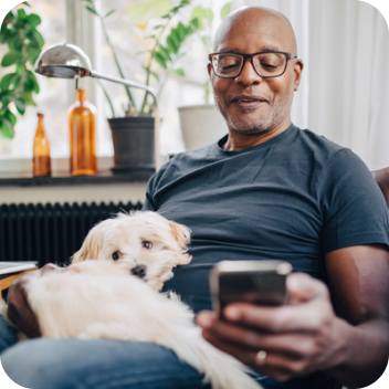 A man using a smartphone with a white dog on his lap