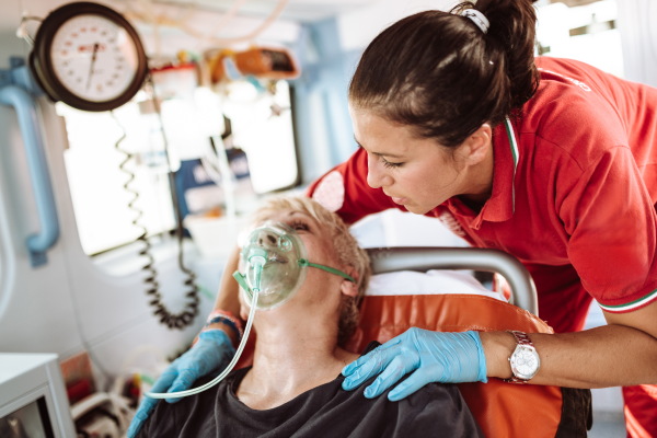 A woman sits in an ambulance with an oxygen mask on, while a paramedic holds her shoulders