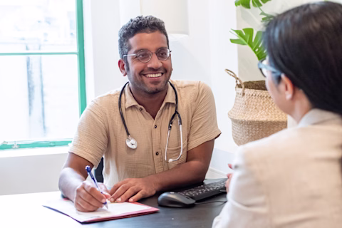 GP smiling kindly at his patient while writing on a piece of paper GP smiling kindly at his patient while writing on a piece of paper