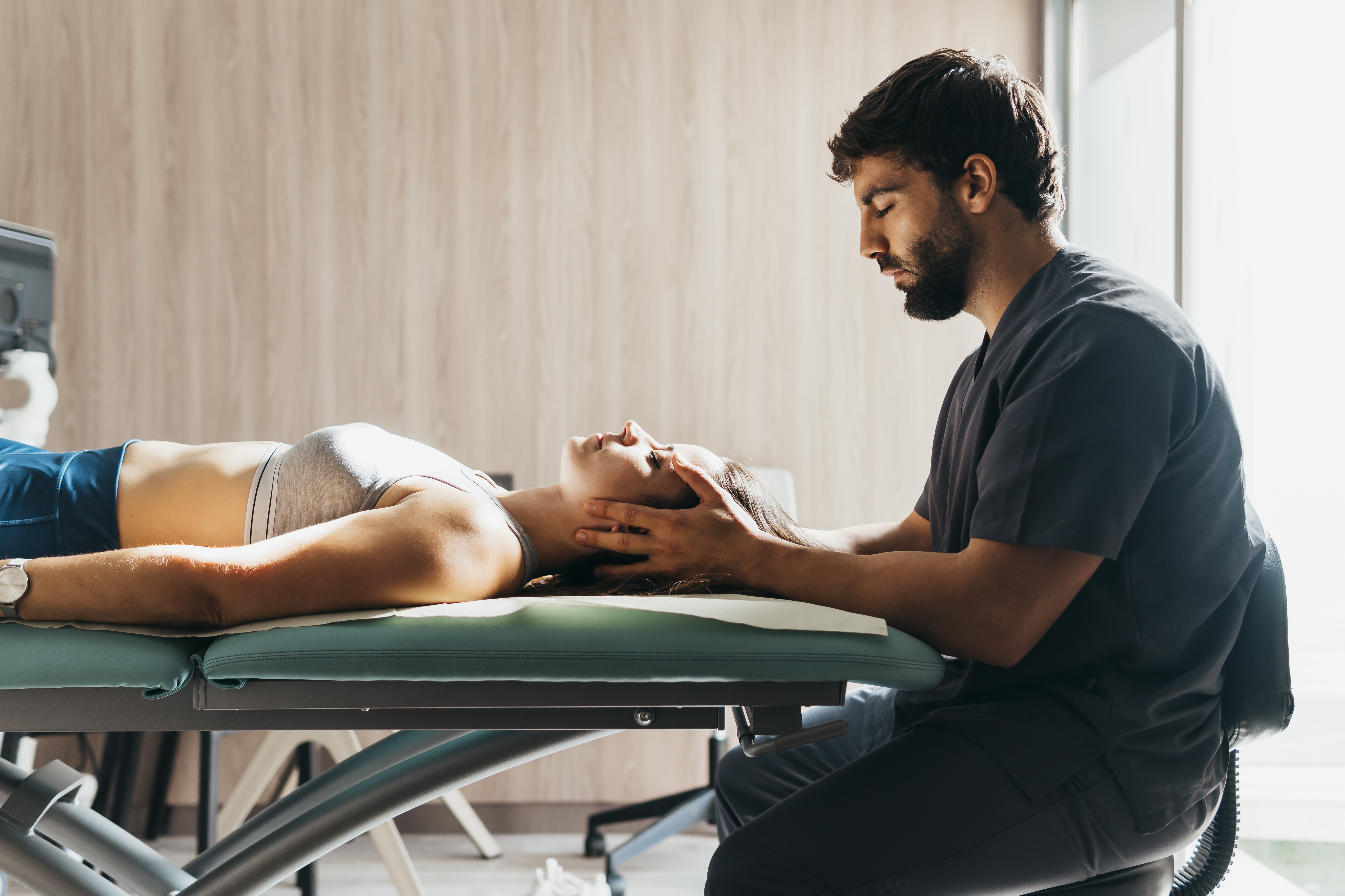 A smiling young man performing exercise with a ball and a physiotherapist