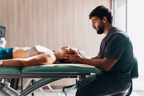 A smiling young man performing exercise with a ball and a physiotherapist